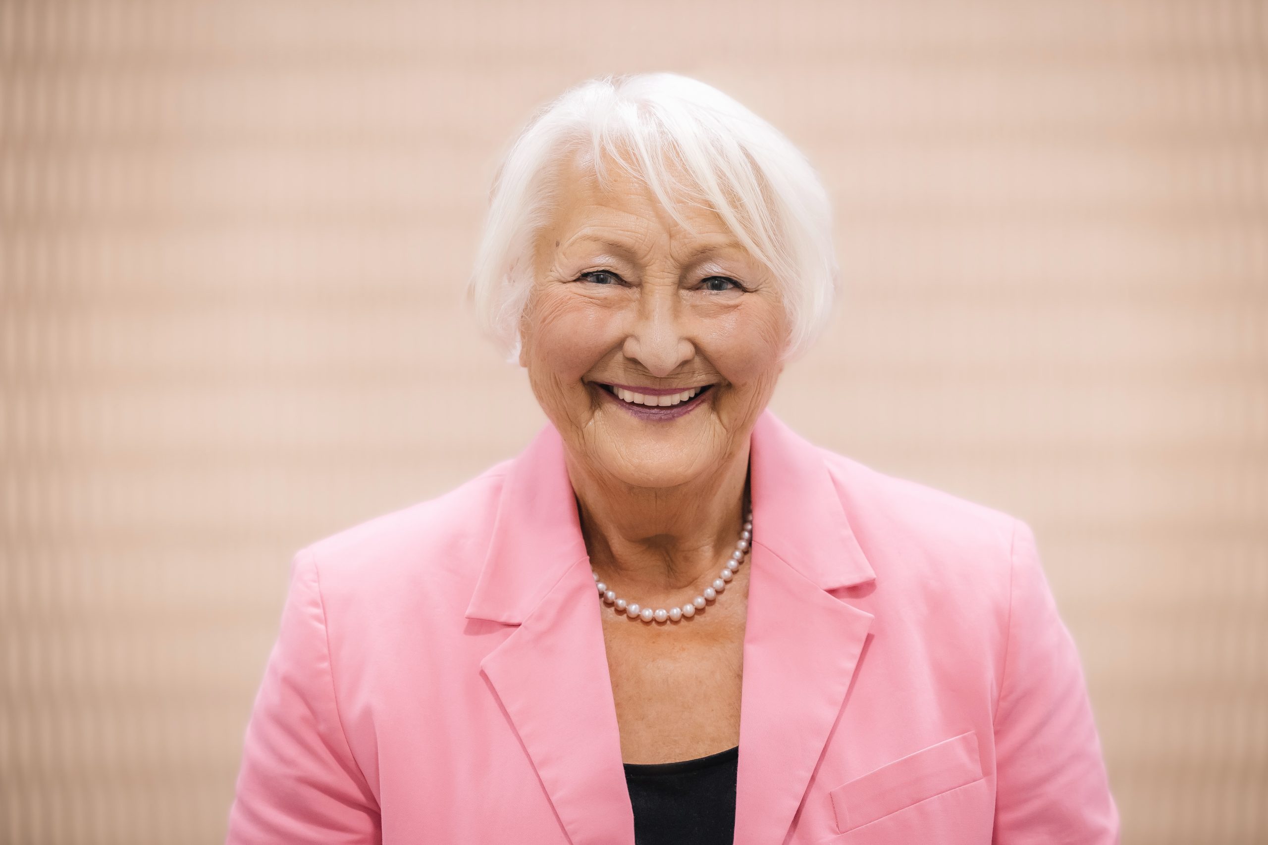 Porträt von einer Frau in einem rosa Blazer mit Perlenkette.
